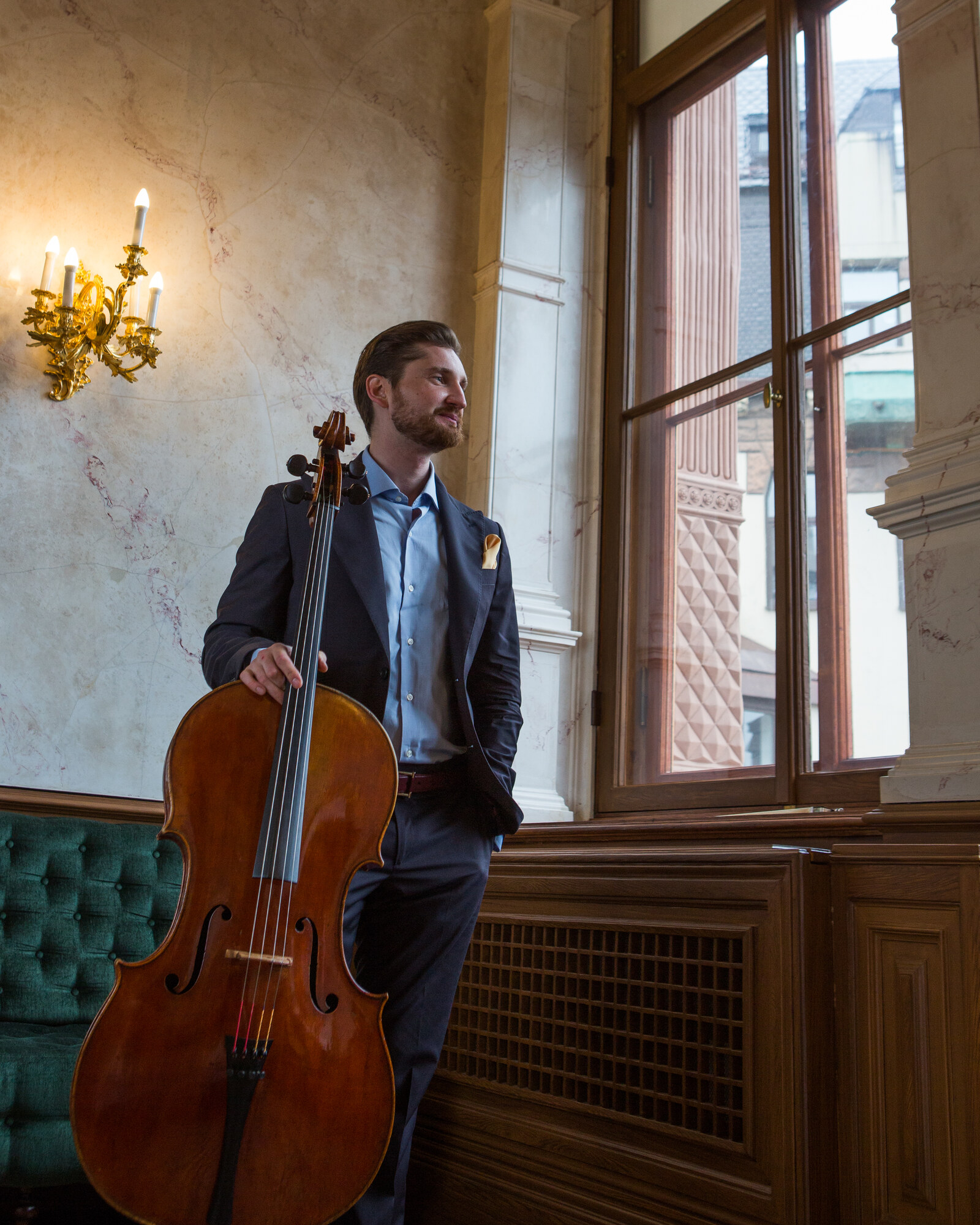 Max Beitan with cello at a palace window, candelabra light.